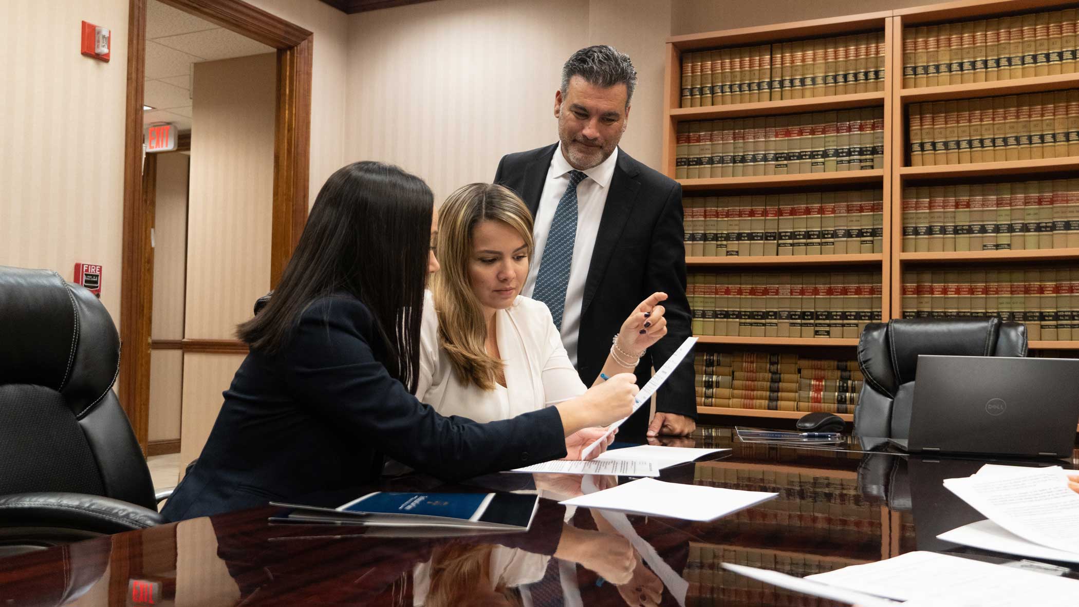 Two female lawyers are seating on a chair and the male lawyer is standing at their side, all are reviewing papers